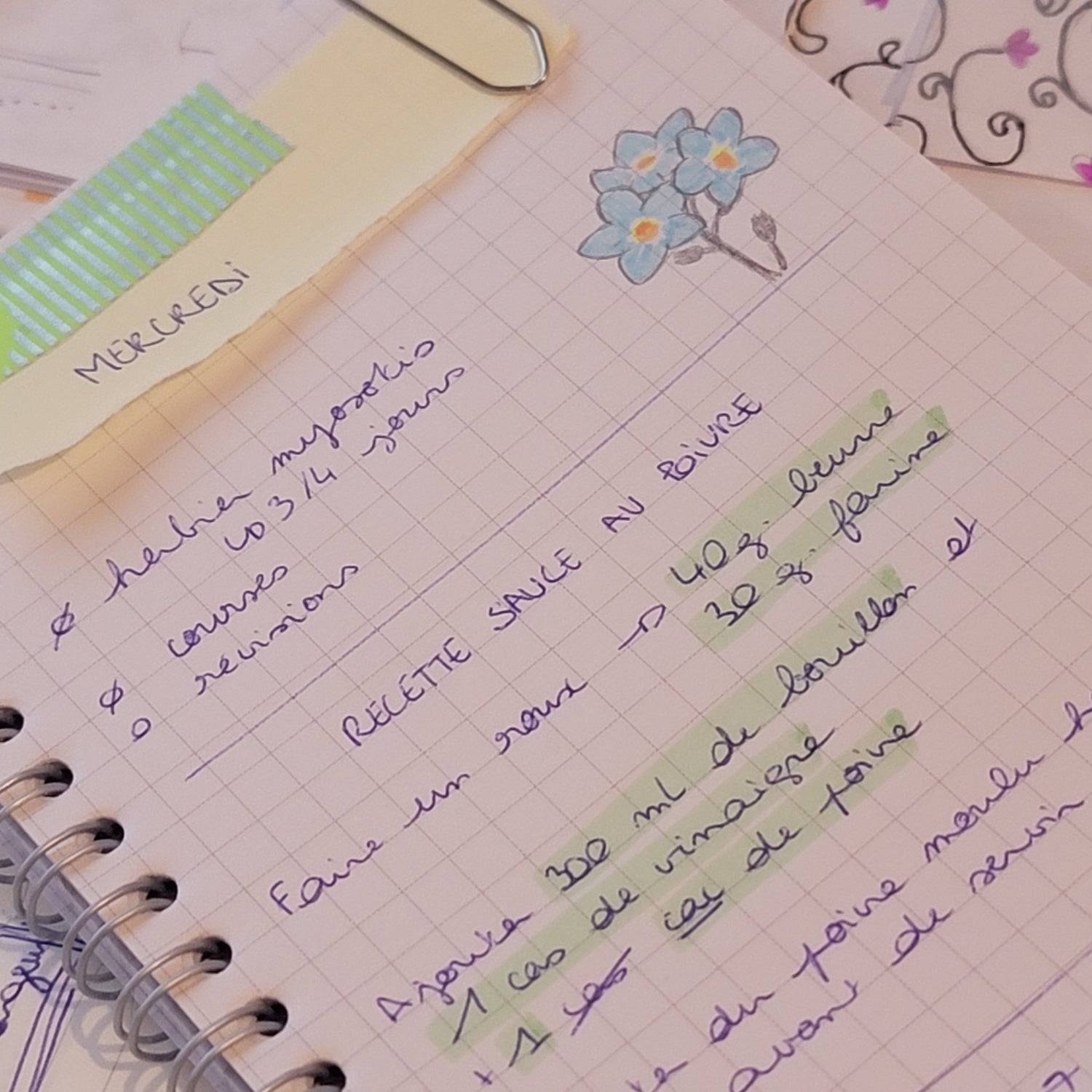 Photographie d'une page de carnet à spirale. La page comporte une liste de choses à faire, un petit dessin de fleur, et une recette écrite sans trop d'attention. Sur le haut de a page, un morceau de papier avec le mot "mercredi" est accroché par du masking tape et un trombone.
